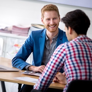 Vertriebsmitarbeiter (m/w/d) haben ein Meeting. Sie sitzen an einem Tisch. Beide haben Unterlagen vor sich